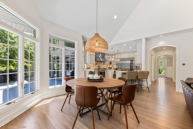 dining room featuring recessed lighting, arched walkways, light wood finished floors, and high vaulted ceiling