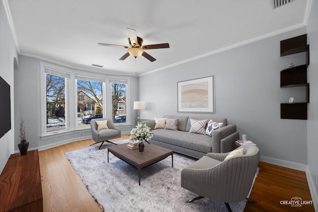 living room with baseboards, visible vents, ceiling fan, wood finished floors, and crown molding