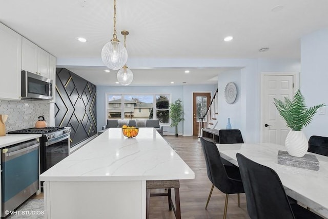 kitchen featuring white cabinets, open floor plan, a center island, hanging light fixtures, and stainless steel appliances