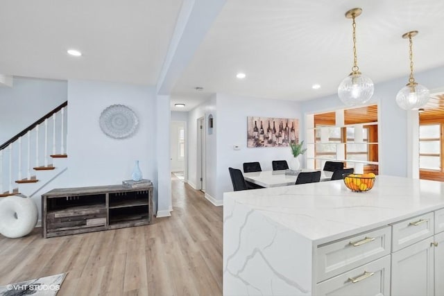 kitchen featuring white cabinets, light wood-style flooring, light stone counters, decorative light fixtures, and recessed lighting