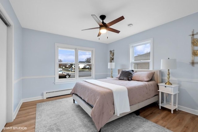 bedroom featuring baseboards, a baseboard heating unit, ceiling fan, and wood finished floors