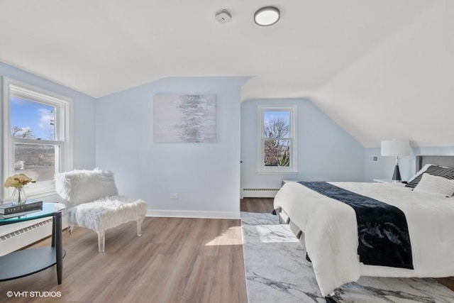 bedroom featuring lofted ceiling, a baseboard radiator, baseboards, and light wood-style floors