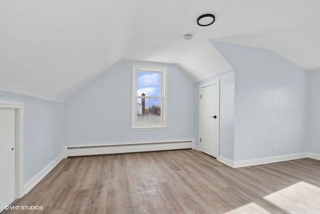 additional living space featuring lofted ceiling, a baseboard radiator, light wood-style flooring, and baseboards