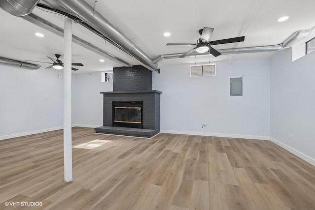 below grade area featuring ceiling fan, visible vents, a brick fireplace, and light wood-style flooring