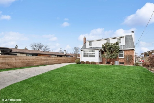 back of house featuring brick siding, a yard, a chimney, and fence