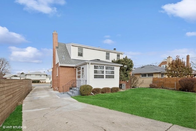 rear view of house featuring a chimney, fence, a lawn, and brick siding