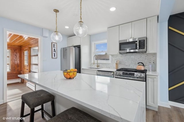 kitchen featuring light stone counters, stainless steel appliances, hanging light fixtures, white cabinetry, and a sink