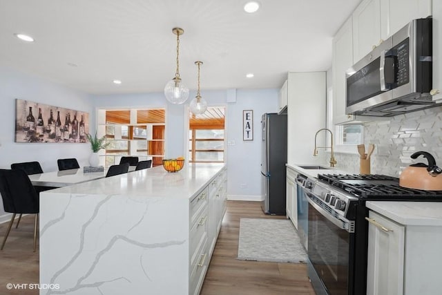 kitchen featuring appliances with stainless steel finishes, a sink, light stone countertops, and white cabinets