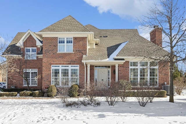 traditional-style home with central air condition unit, brick siding, a chimney, and a shingled roof