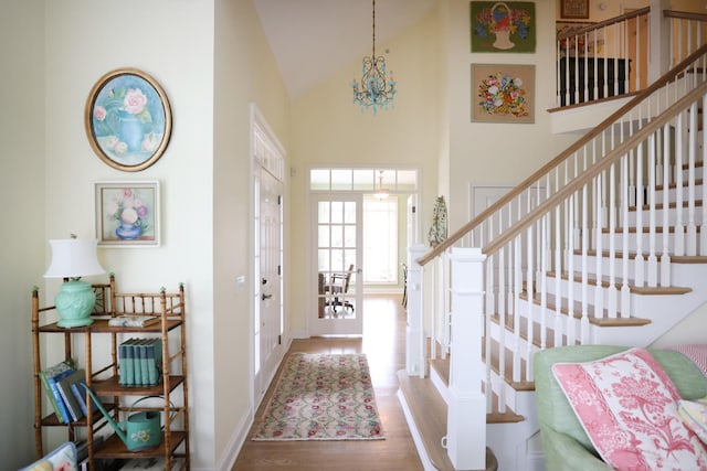 entryway with stairway, high vaulted ceiling, an inviting chandelier, and wood finished floors