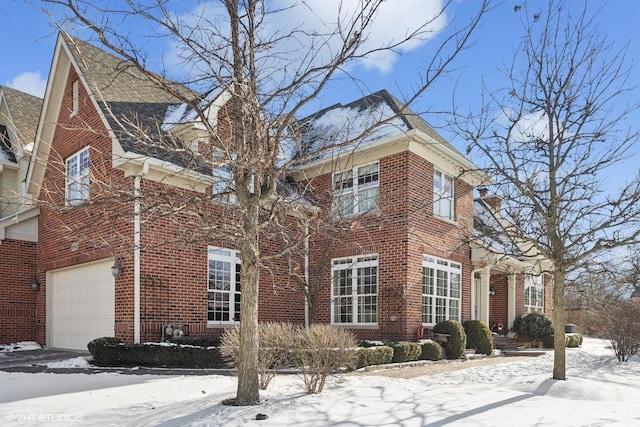 snow covered property with a garage and brick siding