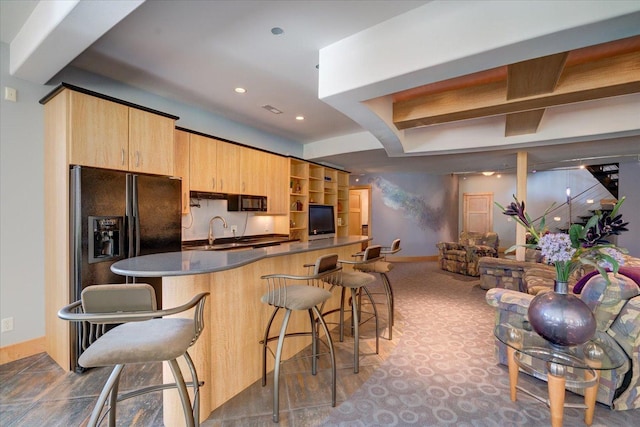 kitchen with a breakfast bar, dark countertops, black refrigerator with ice dispenser, a sink, and baseboards