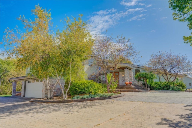 obstructed view of property with a garage, stone siding, and driveway