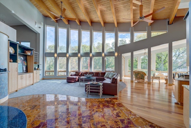 living area with a high ceiling, beamed ceiling, wood ceiling, and a ceiling fan