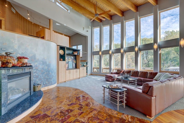 living area featuring wooden ceiling, a high ceiling, beam ceiling, and a glass covered fireplace