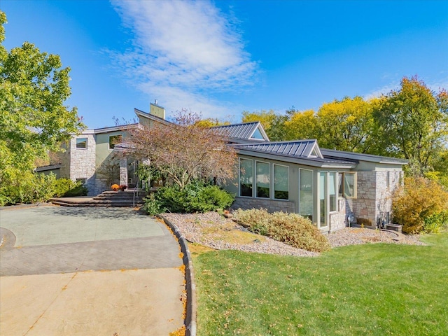 view of front of home with stone siding, a chimney, metal roof, a standing seam roof, and a front lawn