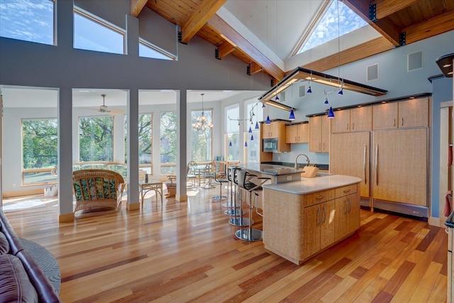 kitchen with pendant lighting, light wood-style flooring, open floor plan, an island with sink, and black microwave