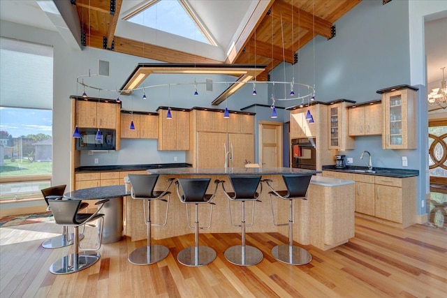 kitchen featuring a spacious island, dark countertops, a towering ceiling, glass insert cabinets, and black appliances