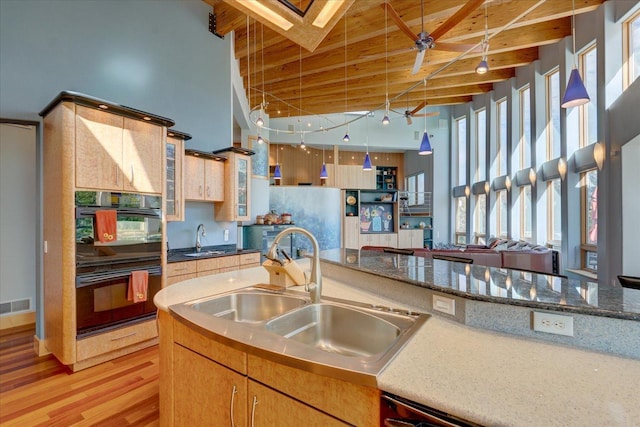 kitchen with dobule oven black, glass insert cabinets, open floor plan, and a sink