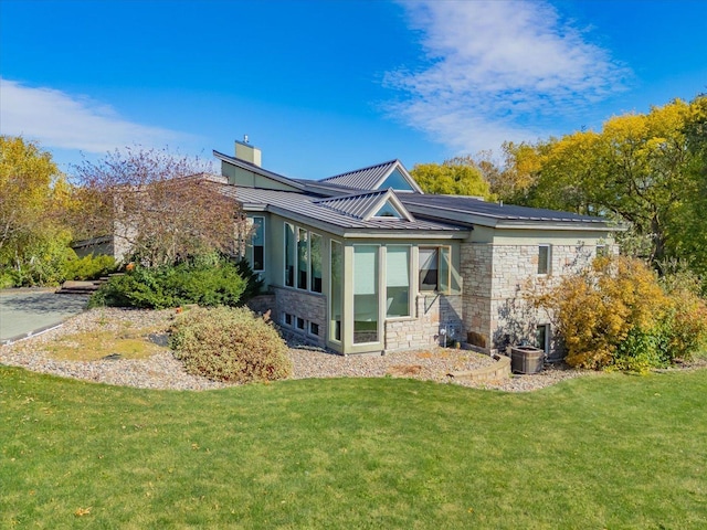 back of house featuring a yard, a standing seam roof, metal roof, cooling unit, and stone siding