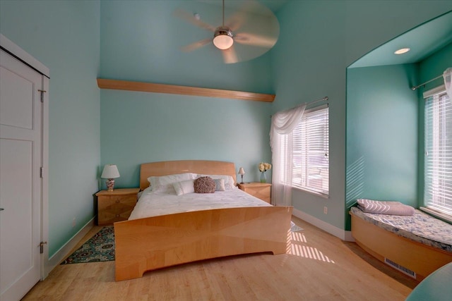 bedroom featuring a towering ceiling, visible vents, light wood-style flooring, and baseboards