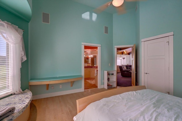 bedroom featuring light wood-style floors, visible vents, a towering ceiling, and baseboards