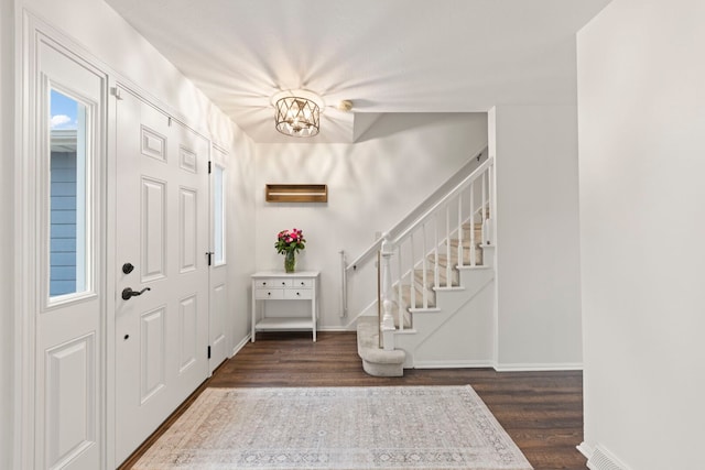 foyer entrance featuring baseboards, stairs, a chandelier, and dark wood-type flooring