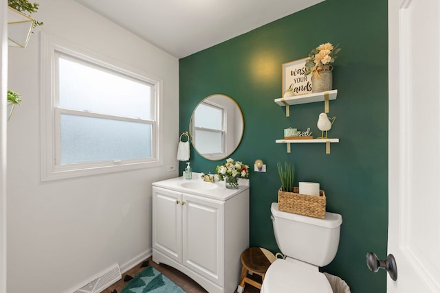 half bathroom with vanity, baseboards, visible vents, and toilet