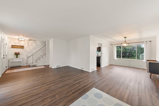 unfurnished living room featuring visible vents, baseboards, stairway, a chandelier, and dark wood finished floors