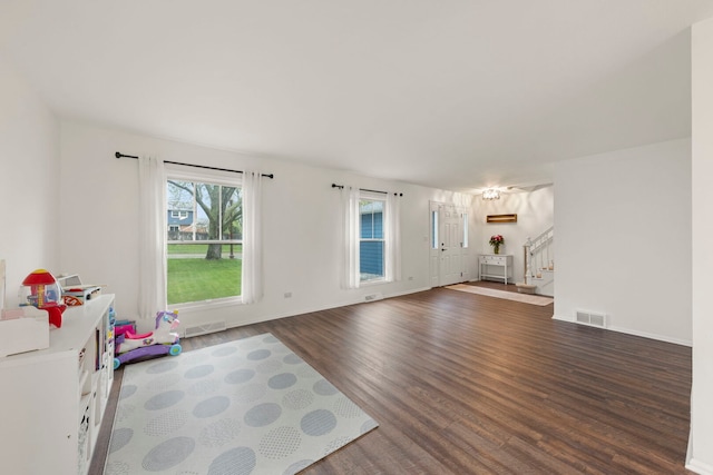 unfurnished living room with baseboards, visible vents, wood finished floors, and stairway