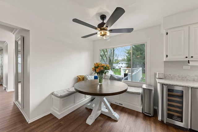 dining room featuring visible vents, beverage cooler, dark wood-type flooring, a bar, and a ceiling fan