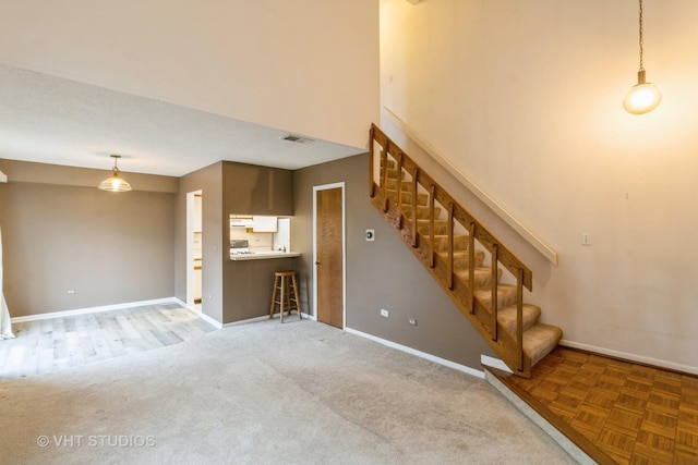 unfurnished living room with stairs, a high ceiling, visible vents, and baseboards