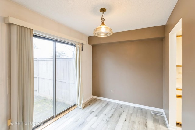 empty room with light wood-style floors, visible vents, baseboards, and a textured ceiling