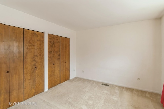 unfurnished bedroom with two closets, visible vents, and light colored carpet