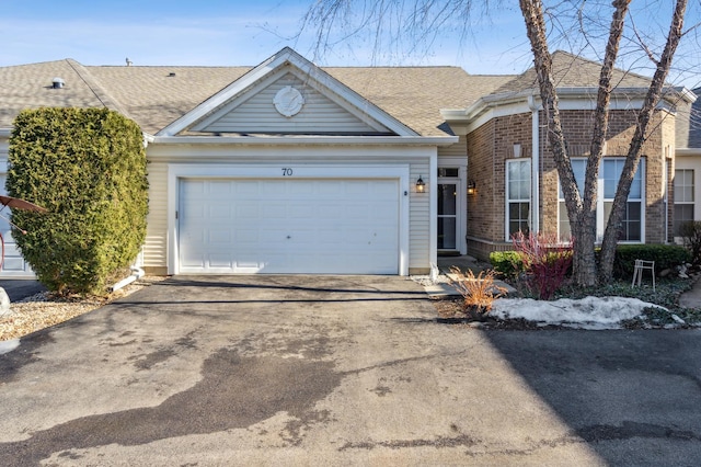 single story home with a garage, driveway, brick siding, and roof with shingles