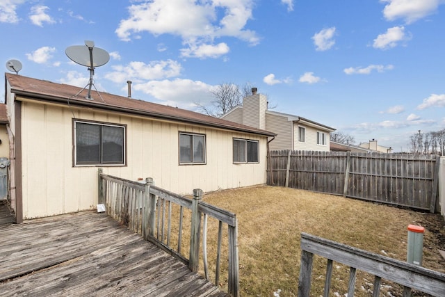 back of property with a fenced backyard, a chimney, a deck, and a yard