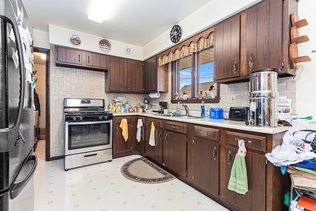 kitchen with stainless steel appliances, a sink, dark brown cabinets, light countertops, and light floors