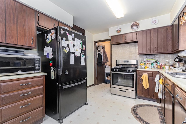 kitchen featuring stainless steel gas range oven, light countertops, freestanding refrigerator, decorative backsplash, and light floors