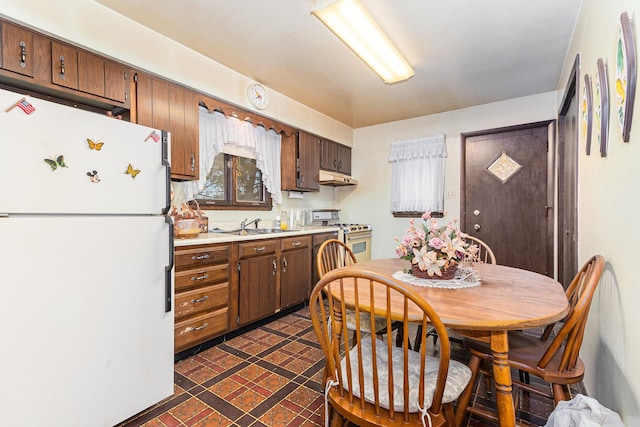 kitchen with light countertops, freestanding refrigerator, a sink, stainless steel gas range, and under cabinet range hood