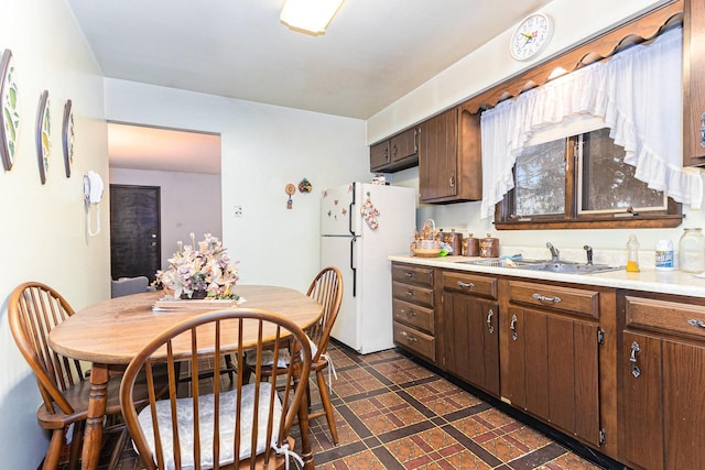 kitchen with light countertops, a sink, freestanding refrigerator, and dark brown cabinetry