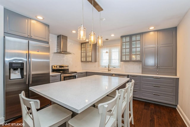 kitchen featuring a sink, appliances with stainless steel finishes, wall chimney range hood, a center island, and glass insert cabinets