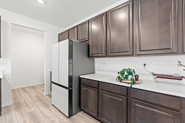 kitchen featuring light wood-type flooring, dark brown cabinetry, light countertops, and freestanding refrigerator