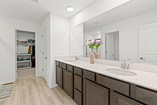 full bathroom featuring double vanity, visible vents, a sink, and wood finished floors