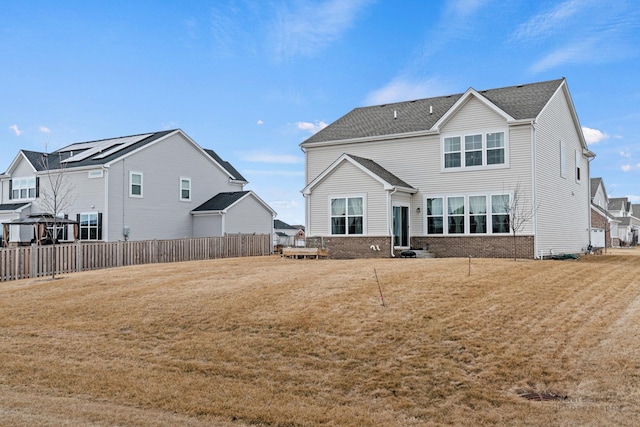 rear view of house featuring roof with shingles, fence, a lawn, and brick siding