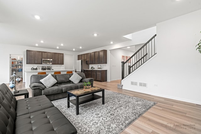 living area featuring visible vents, baseboards, light wood-style flooring, stairs, and recessed lighting