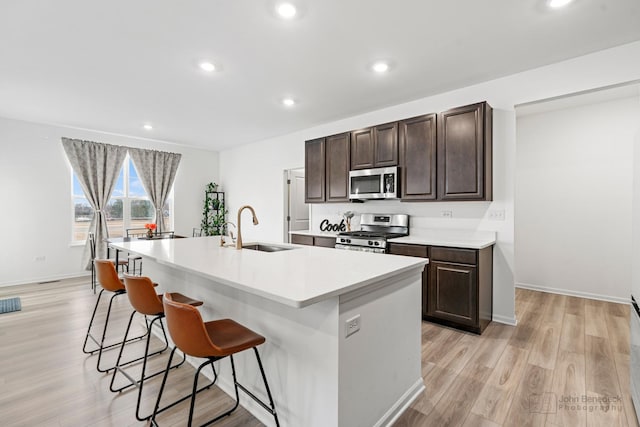 kitchen with a breakfast bar, stainless steel appliances, light countertops, a kitchen island with sink, and a sink