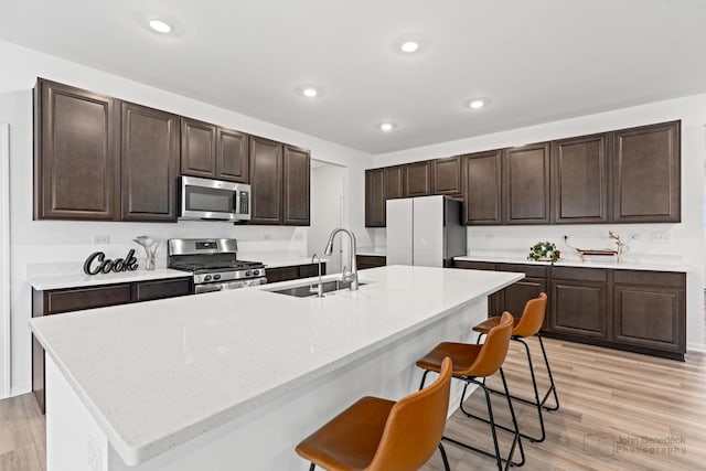 kitchen with stainless steel appliances, a breakfast bar, light wood-type flooring, and a sink