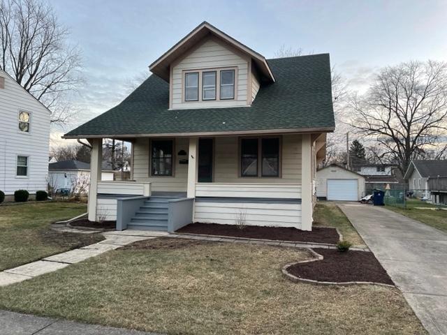 bungalow featuring driveway, a garage, a porch, an outbuilding, and a front lawn