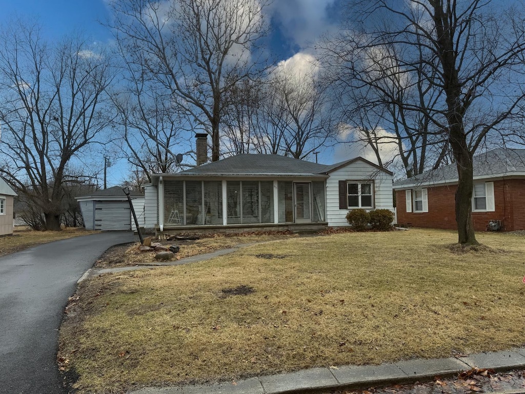 single story home with a sunroom, a front yard, aphalt driveway, and an outbuilding