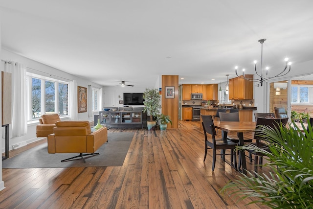 dining space with ceiling fan with notable chandelier, wood-type flooring, visible vents, and a healthy amount of sunlight